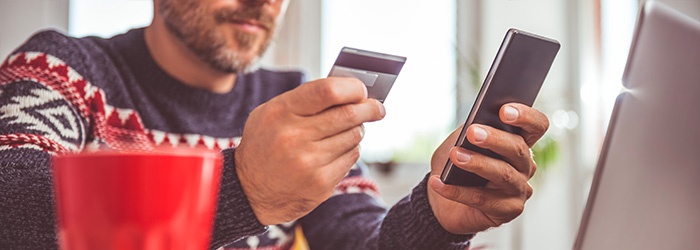 Men-holding-credit-card-and-using-smart-phone-at-home-office-868966516_700x250