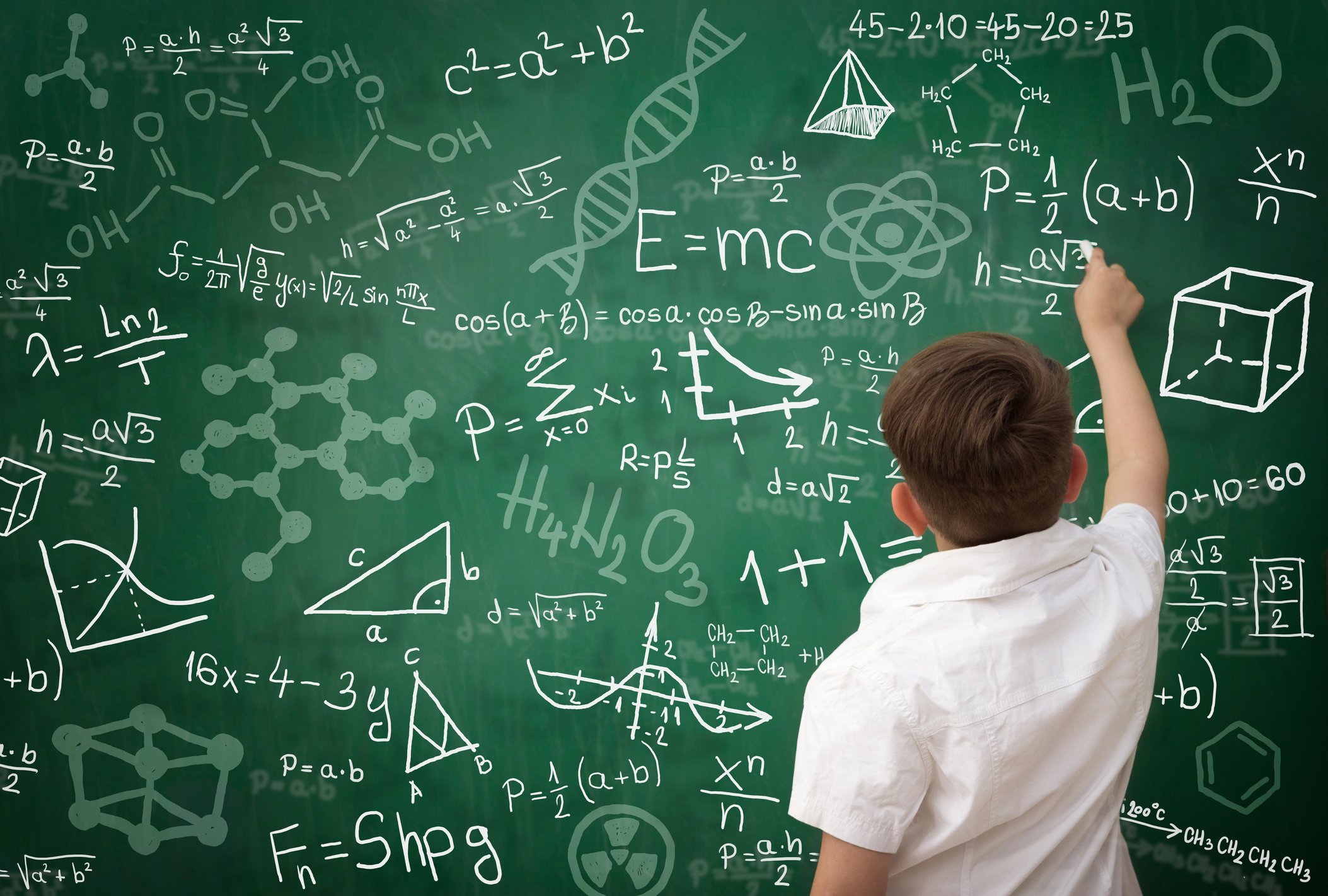 Back view of schoolboy writing math formula on green blackboard