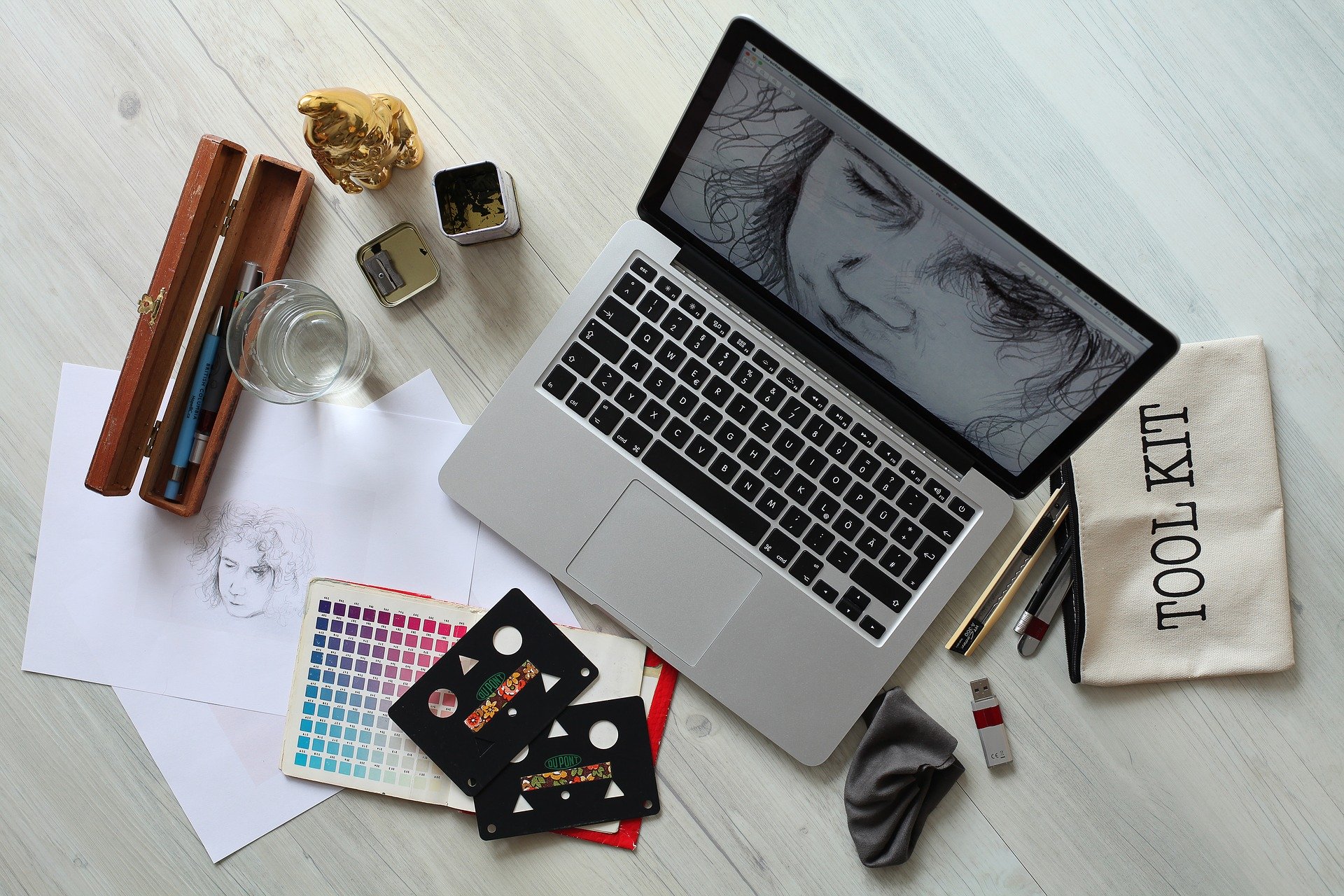 A laptop showing a sketch with a color palette and graphic design tools around it.