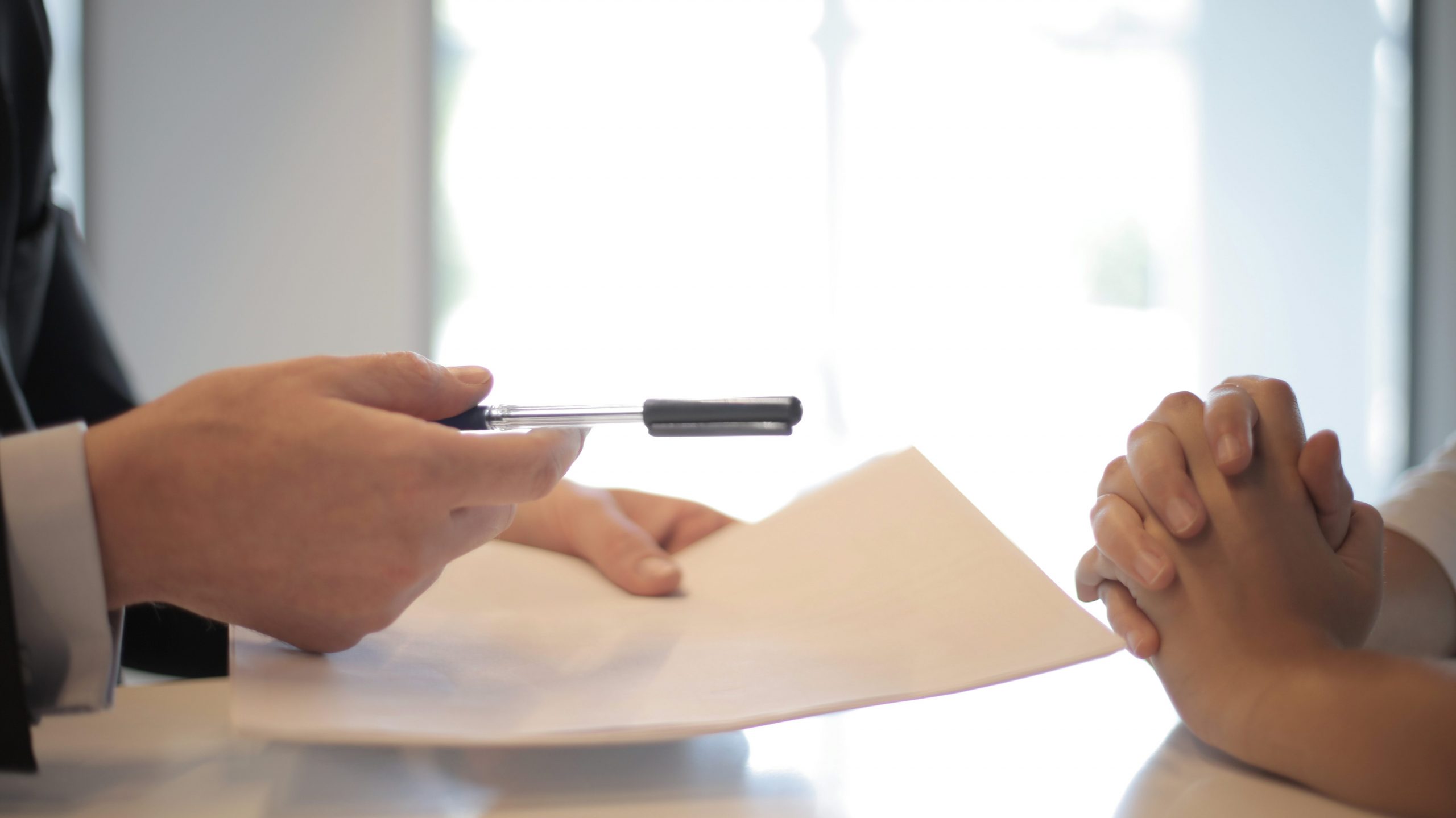 A businessman hands a piece of paper and a pen to their employee to sign