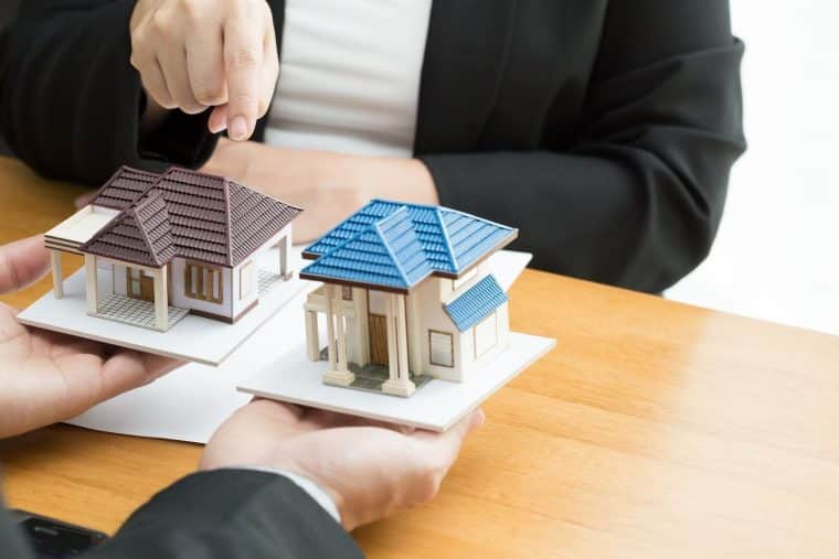 2 small houses on a desk with someone pointing at them