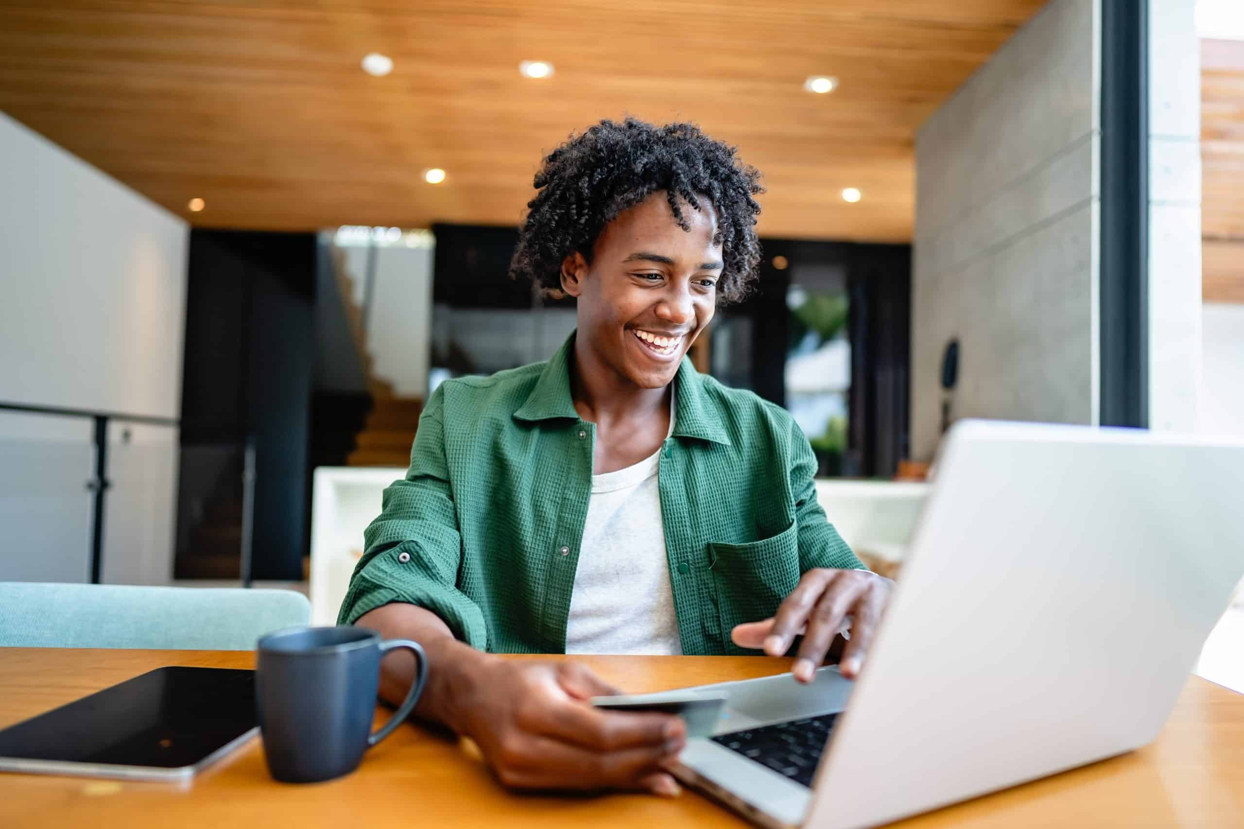 man with card in hand at laptop smiling